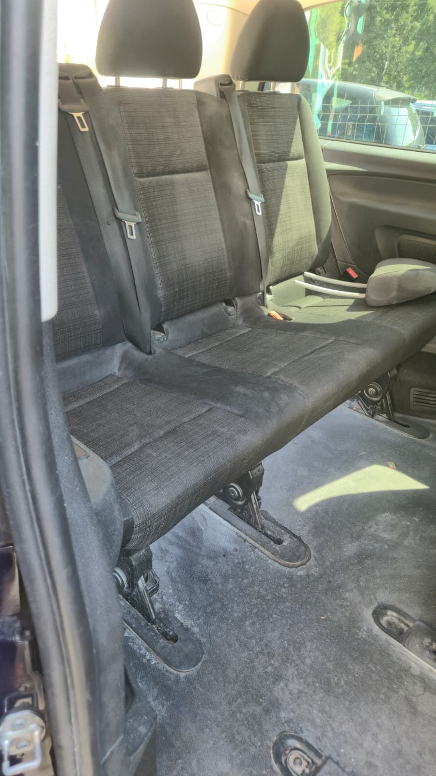 Bancheta din rândul doi al unui Mercedes Vito, văzută din ușa glisantă. Pe material se văd pete întinse, iar mocheta de pe podea și șinele scaunelor sunt acoperite cu un praf alb.